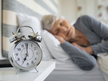 Persona mayor durmiendo y en primer plano un despertador