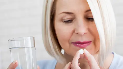 Mujer tomándose una pastilla para los síntomas de la menopausia Mujer tomándose una pastilla para los síntomas de la menopausia
