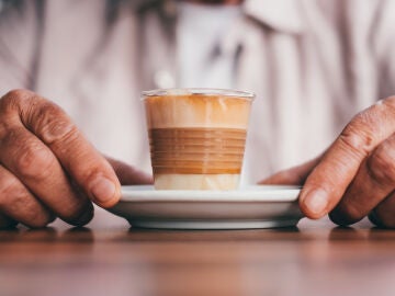 Manos de hombre mayor rodeando un vaso de caf&eacute;