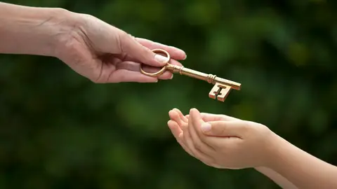 Mano mujer dando una llave a una mano joven Mano mujer dando una llave a una mano joven