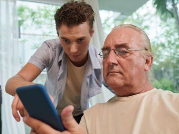 Joven ayudando a una persona mayor con el tel&eacute;fono m&oacute;vil