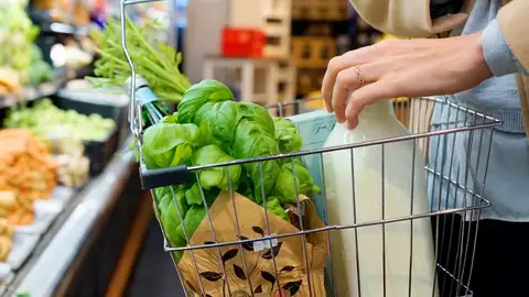 Una persona compra en un supermercado con una cesta que contiene verduras frescas, leche y hierbas. Una persona compra en un supermercado con una cesta que contiene verduras frescas, leche y hierbas.