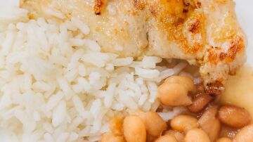 Primer plano de un delicioso pollo a la parrilla servido con arroz y frijoles en un plato.
